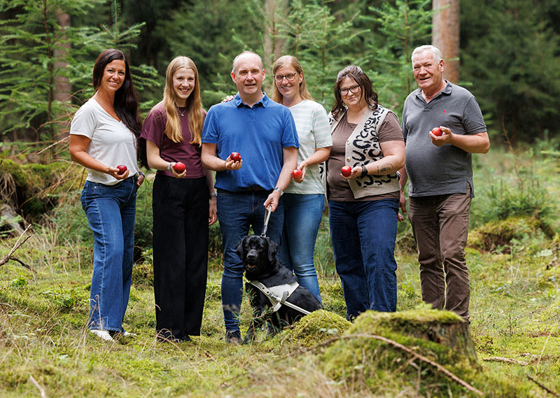 Das Team von Apfel-Fleger mit Äpfeln und Ella im Wald